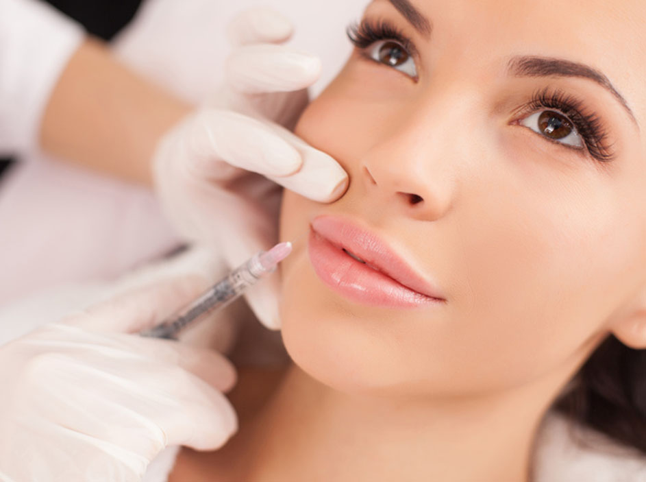 Close up of hands of cosmetologist making botox injection in female lips. She is holding syringe. The young beautiful woman is receiving procedure with enjoyment